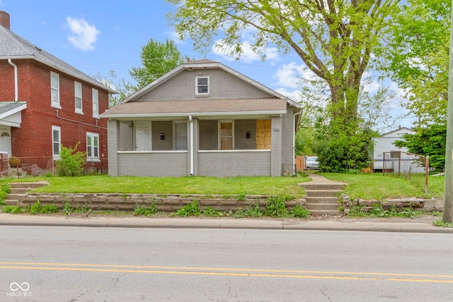 view of front of home with covered porch, brick siding, and a front yard