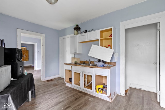 kitchen featuring a sink, white cabinetry, baseboards, and wood finished floors