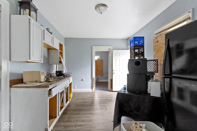 kitchen featuring a sink, wood finished floors, freestanding refrigerator, white cabinets, and baseboards