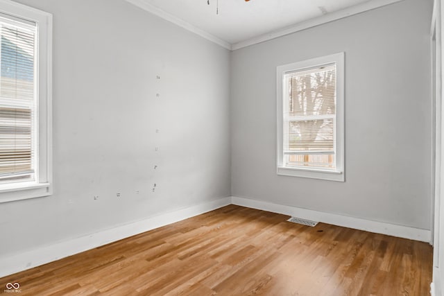 empty room with crown molding, visible vents, baseboards, and light wood finished floors