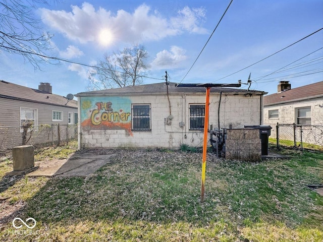 rear view of house with concrete block siding, fence, and a lawn