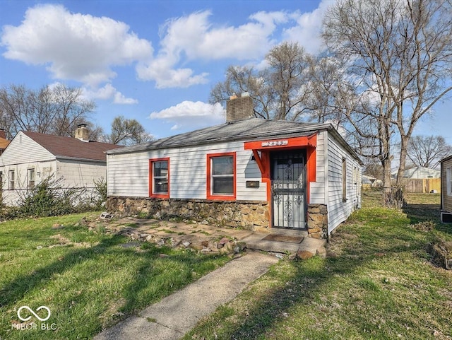 view of front of home with stone siding, a chimney, fence, and a front yard