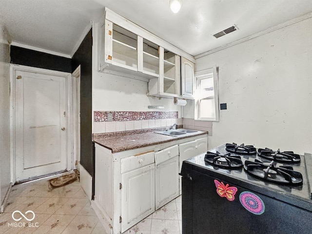 kitchen featuring white cabinets, visible vents, ornamental molding, dark countertops, and a sink