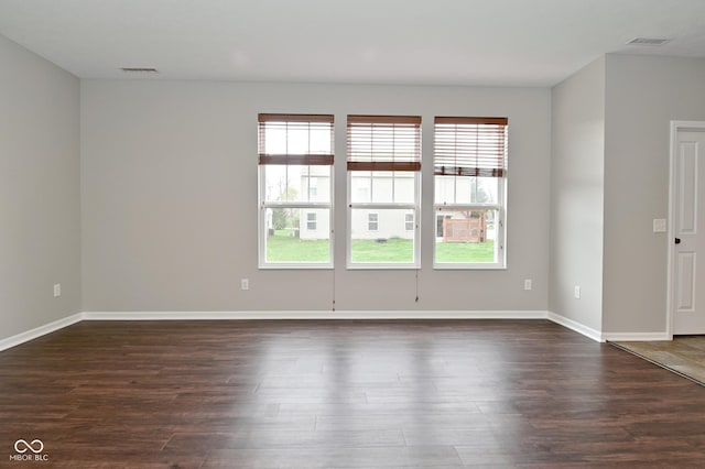 empty room featuring dark wood finished floors, visible vents, baseboards, and a healthy amount of sunlight