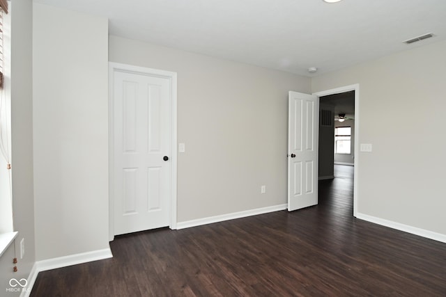 unfurnished room featuring dark wood-type flooring, visible vents, and baseboards