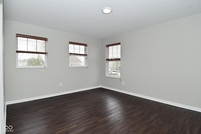 unfurnished room with baseboards and dark wood-style floors