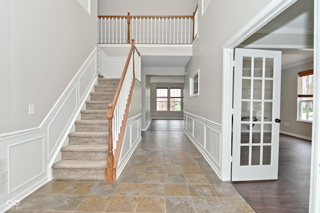 foyer entrance with stairway, a wainscoted wall, stone finish floor, ornamental molding, and a decorative wall