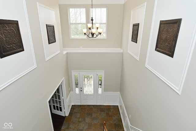 entryway featuring a towering ceiling, stone finish floor, and a notable chandelier