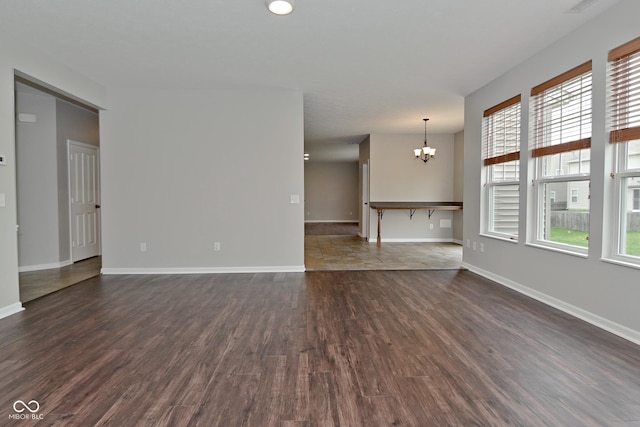 unfurnished living room featuring baseboards, dark wood-style floors, and a chandelier