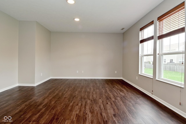 spare room featuring dark wood-type flooring, a healthy amount of sunlight, and baseboards
