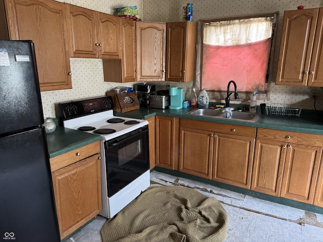 kitchen featuring wallpapered walls, brown cabinets, range with electric cooktop, a sink, and freestanding refrigerator