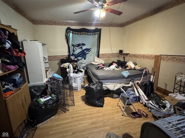 bedroom with a wainscoted wall, wood finished floors, and a ceiling fan