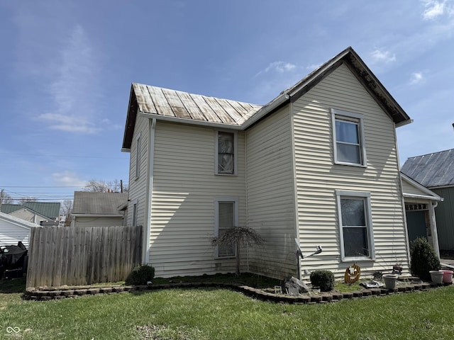 back of house featuring fence, metal roof, a standing seam roof, and a yard
