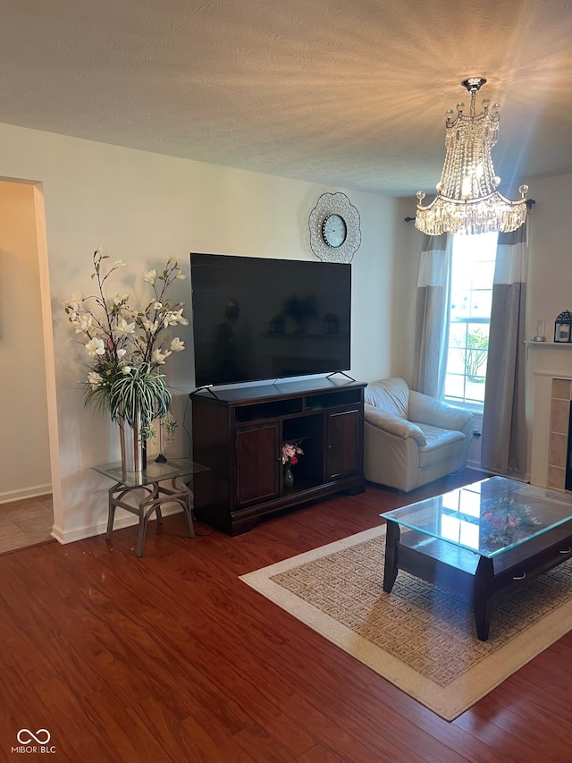 living room featuring a textured ceiling, a fireplace, wood finished floors, baseboards, and a chandelier