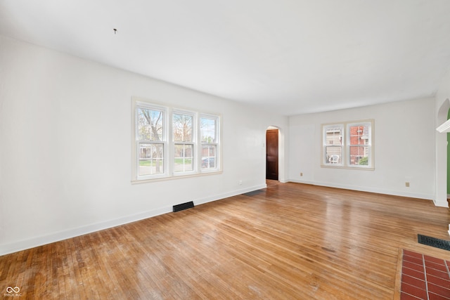 unfurnished living room featuring a wealth of natural light, arched walkways, and light wood-style floors