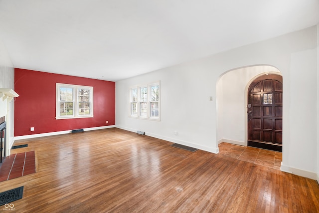 unfurnished living room featuring a fireplace with flush hearth, arched walkways, wood finished floors, and visible vents
