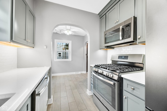 kitchen with stainless steel appliances, arched walkways, light countertops, and gray cabinets