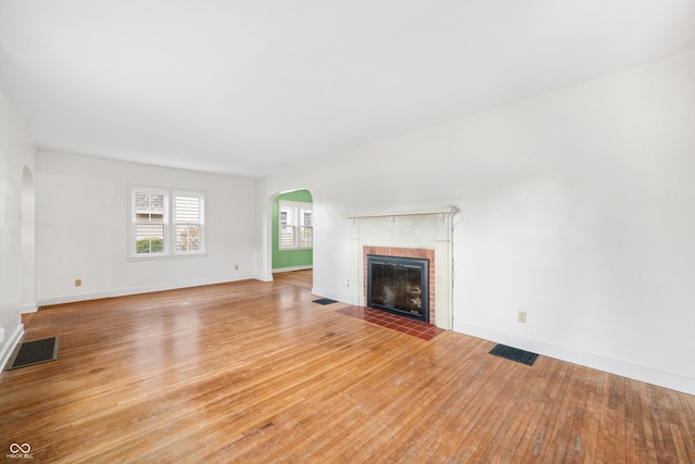 unfurnished living room with a fireplace, arched walkways, light wood finished floors, and visible vents