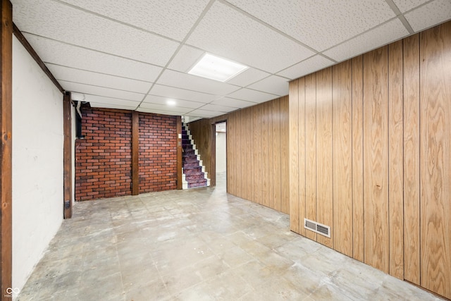 finished basement with a paneled ceiling, tile patterned floors, stairway, wood walls, and visible vents