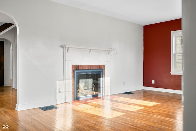 unfurnished living room featuring arched walkways, visible vents, a brick fireplace, baseboards, and hardwood / wood-style flooring