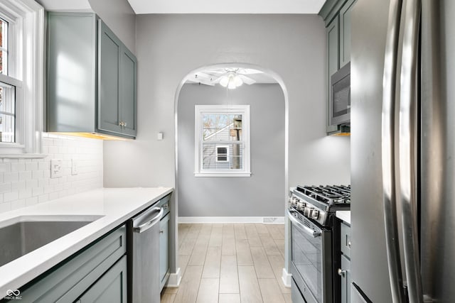 kitchen featuring gray cabinets, decorative backsplash, arched walkways, and stainless steel appliances