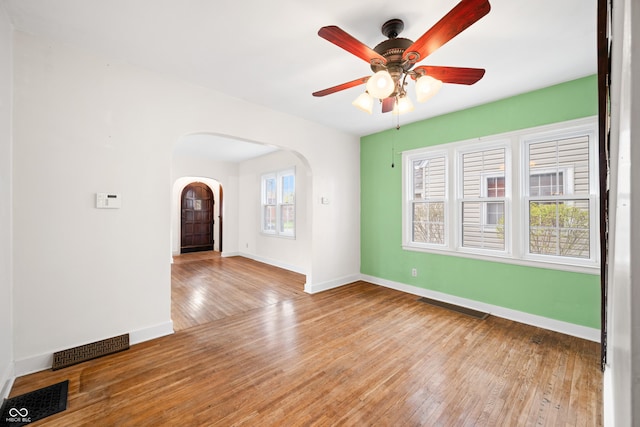 empty room with visible vents, baseboards, arched walkways, and hardwood / wood-style flooring