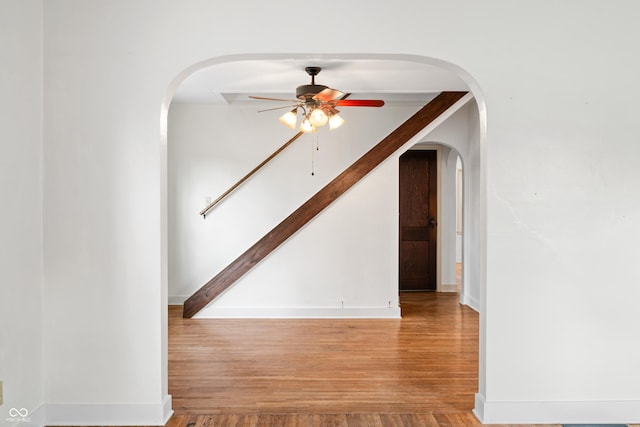 spare room featuring ceiling fan, arched walkways, wood finished floors, and baseboards