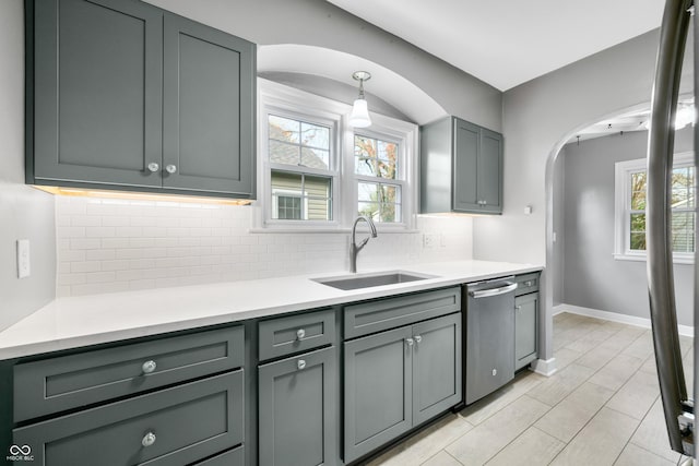 kitchen with arched walkways, a sink, light countertops, backsplash, and stainless steel dishwasher