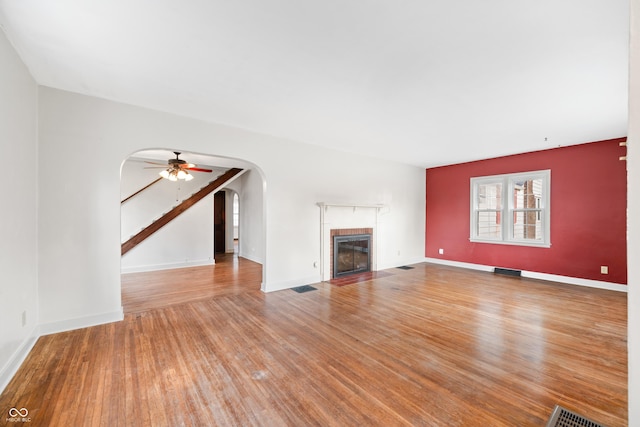 unfurnished living room featuring visible vents, arched walkways, ceiling fan, a fireplace, and wood finished floors