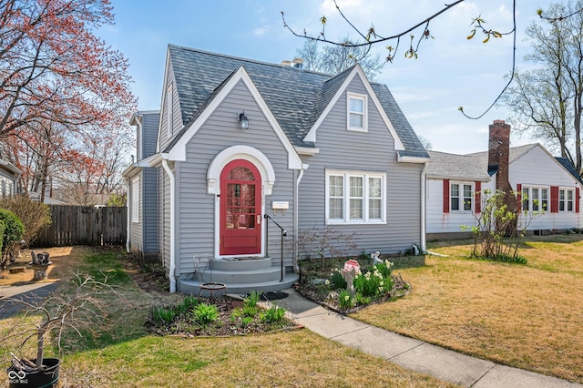 view of front facade featuring a front yard, fence, and a shingled roof