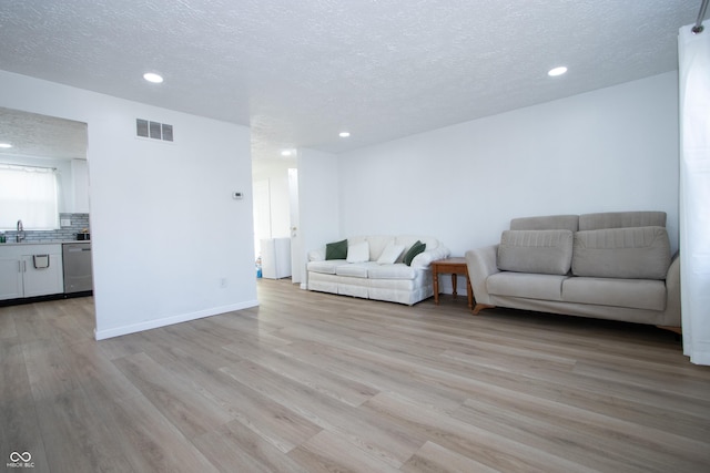 living room featuring recessed lighting, a textured ceiling, visible vents, and light wood-style flooring