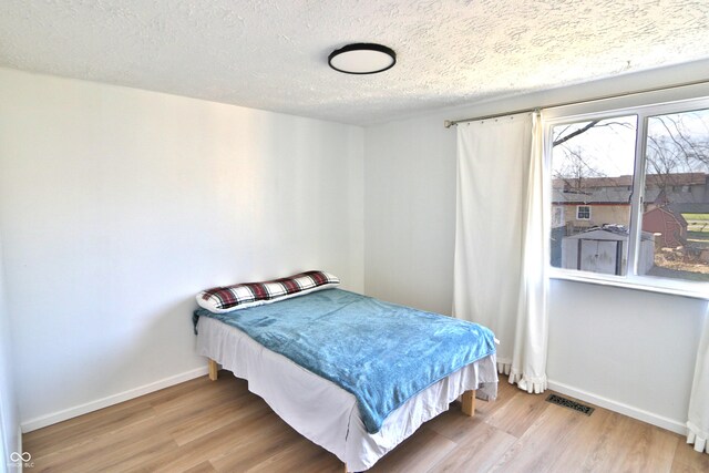 bedroom with wood finished floors, visible vents, a textured ceiling, and baseboards