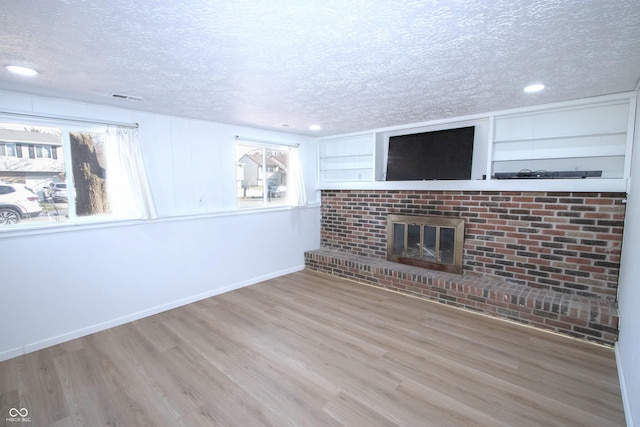 unfurnished living room featuring wood finished floors, a fireplace, baseboards, visible vents, and a textured ceiling
