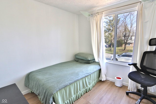 bedroom with a textured ceiling, wood finished floors, and baseboards