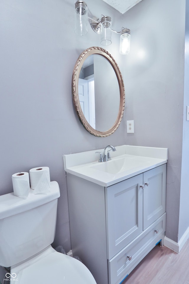 half bathroom featuring wood finished floors, toilet, vanity, and baseboards
