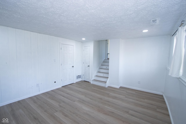 below grade area featuring visible vents, stairway, wood finished floors, and a textured ceiling
