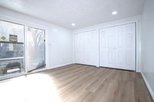 unfurnished bedroom with access to outside, multiple closets, wood finished floors, and baseboards