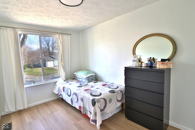 bedroom featuring baseboards, visible vents, wood finished floors, and a textured ceiling