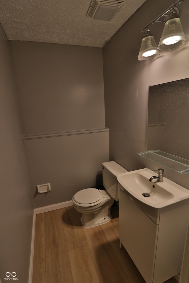 bathroom with a textured ceiling, visible vents, toilet, wood finished floors, and vanity