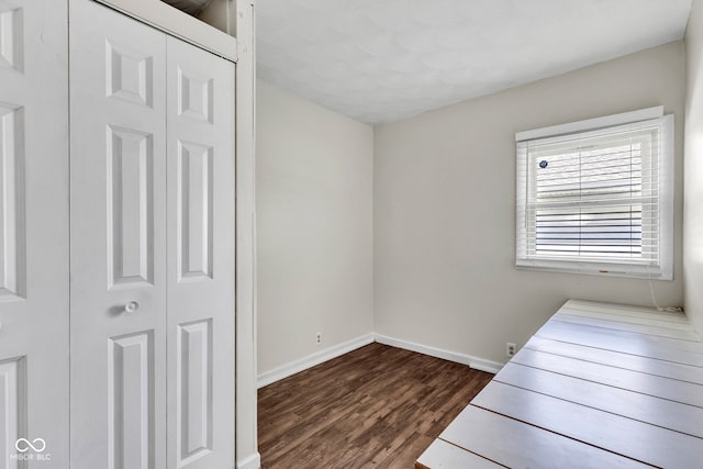 unfurnished bedroom with baseboards, a closet, and dark wood finished floors