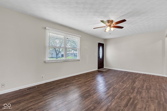 unfurnished room featuring ceiling fan, a textured ceiling, baseboards, dark wood-type flooring, and visible vents