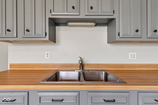kitchen with gray cabinetry, wooden counters, and a sink