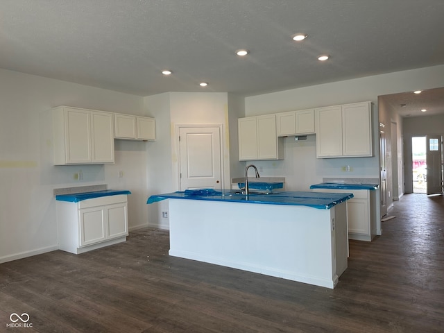 kitchen featuring baseboards, dark wood-style flooring, white cabinets, and a center island with sink