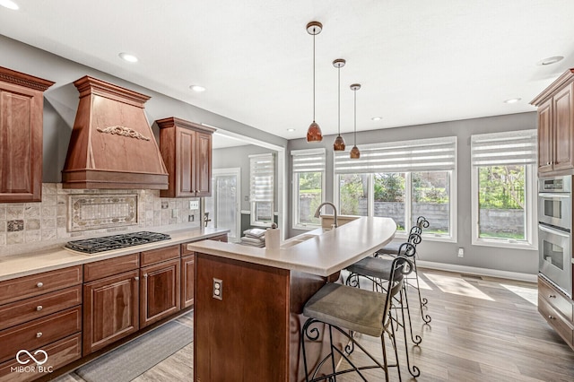 kitchen featuring a breakfast bar area, light countertops, backsplash, light wood finished floors, and premium range hood