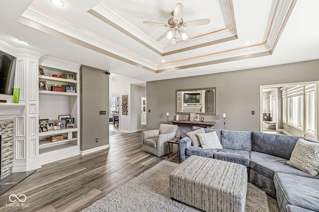 living room featuring built in features, a tray ceiling, crown molding, a ceiling fan, and wood finished floors
