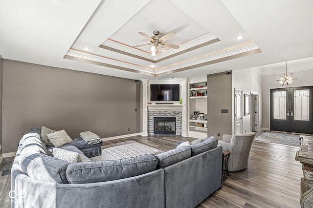 living area with baseboards, ornamental molding, dark wood-style floors, a ceiling fan, and a tray ceiling