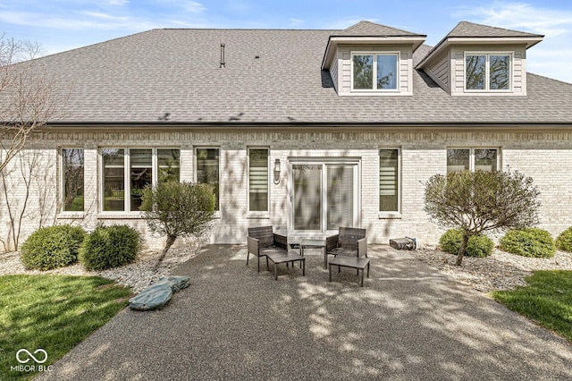 rear view of house with brick siding, a shingled roof, and a patio area