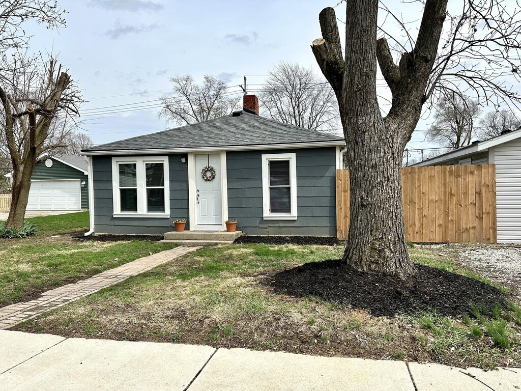410 Spann Ave, Crawfordsville, IN 47933 - bungalow with fence, a chimney, a front lawn, a shingled roof, and an outdoor structure