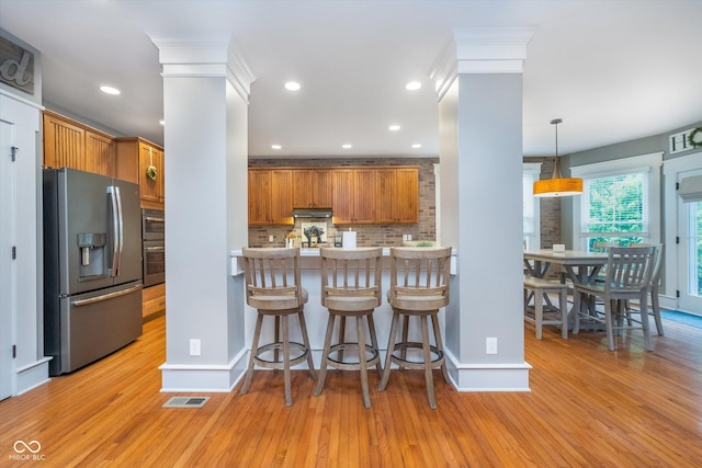 2353 Woodcreek Crossing Blvd, Avon, IN 46123 - kitchen with stainless steel fridge with ice dispenser, decorative backsplash, light wood-type flooring, brown cabinets, and under cabinet range hood