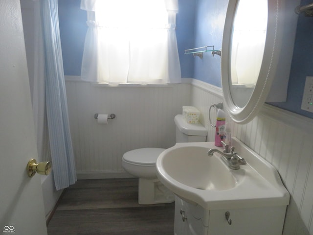 full bath with toilet, curtained shower, vanity, wood finished floors, and wainscoting